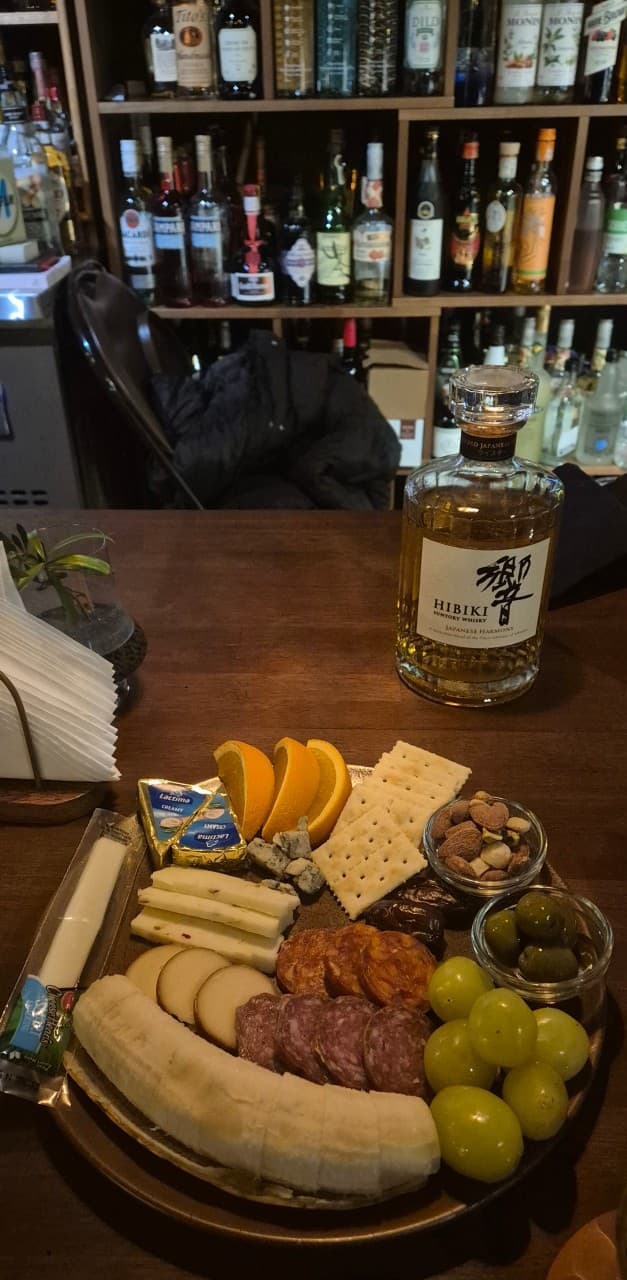대전광역시 서구 탱이 대전 바(Bar) 다찌석의 혼술 세팅. 조명 아래 히비키 위스키와 과일, 치즈, 크래커가 담긴 플래터가 나무 테이블 위에 놓인 구성.