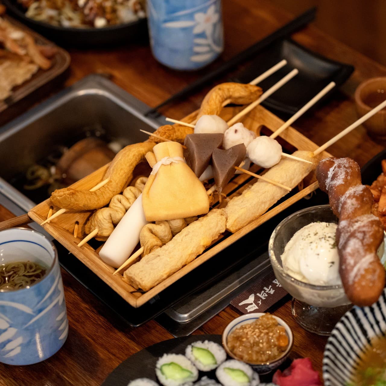 대전광역시 서구 요리주점 철길부산집 가수원점 대전 1인 다찌석 어묵 세트. 조명 아래 나무 테이블 위로 놓인 어묵 꼬치와 유부 주머니, 아이스크림과 꽈배기 질감이 강조된 혼술 차림상.