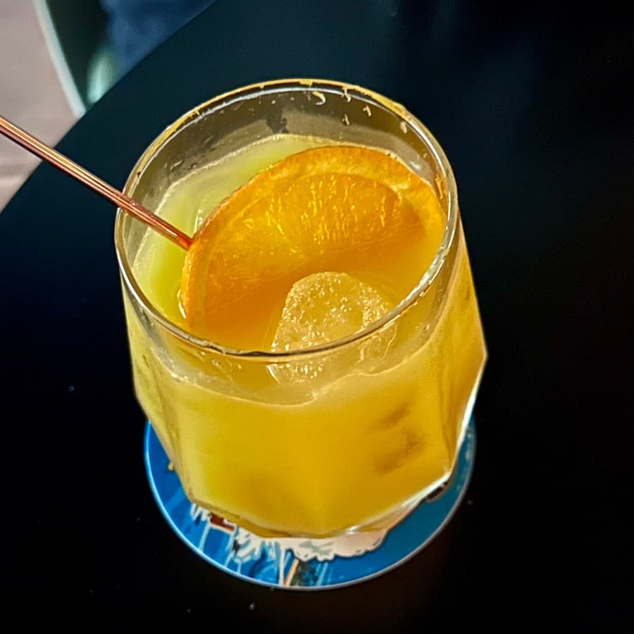경상북도 포항시 이스트사이드뮤직 경북 바(Bar) 블랙 테이블 위 오렌지 가니쉬를 곁들인 노란 칵테일과 블루 코스터. 1인 다찌석에서 즐기는 혼술 상황.