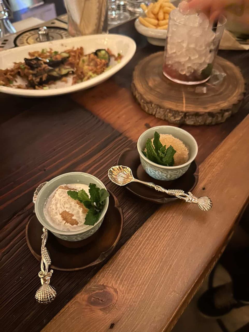경상북도 경주시 바분 월정교점 경북 바(Bar) 나무 다찌석 위 민트 잎을 얹은 디저트와 조개 문양 스푼, 얼음 가득한 칵테일이 차려진 혼술 테이블