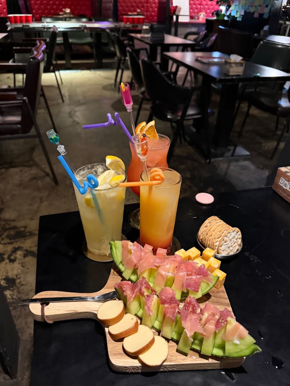 경상북도 경산시 혼술 바(Bar) 비사이드 경북 - 어두운 조명 아래 1인 테이블 위 멜론 하몽과 치즈 플래터, 알록달록한 칵테일이 차려진 현장