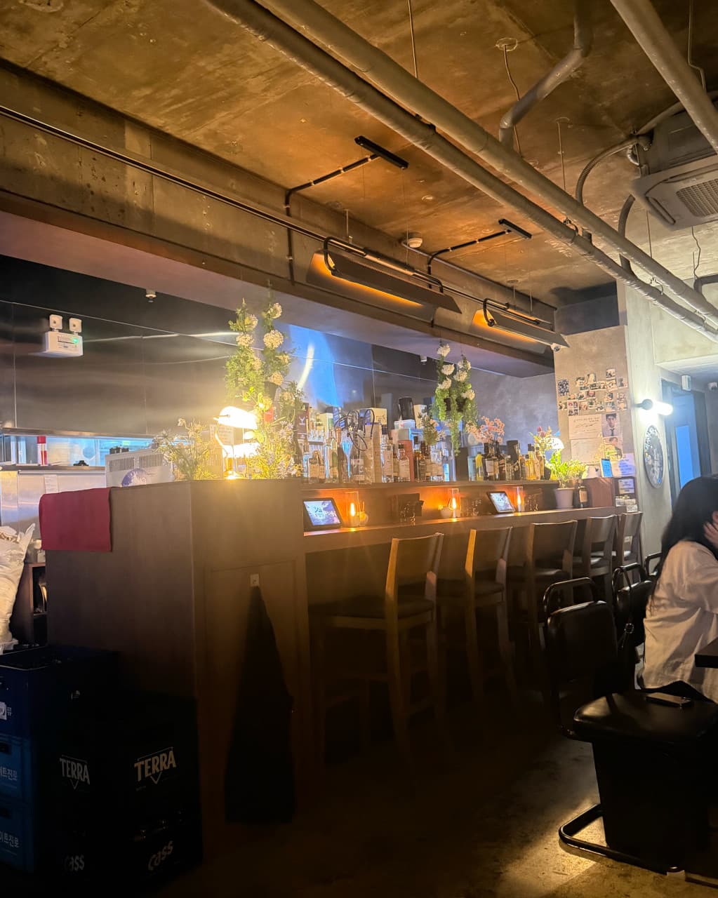 경기도 화성시 식사가되는 술집 양심 동탄점 경기 요리주점. 주황색 조명 아래 마련된 다찌석과 1인 바 테이블. 노출 천장과 진열된 술병들 사이에서 태블릿으로 주문하며 혼술하는 공간.