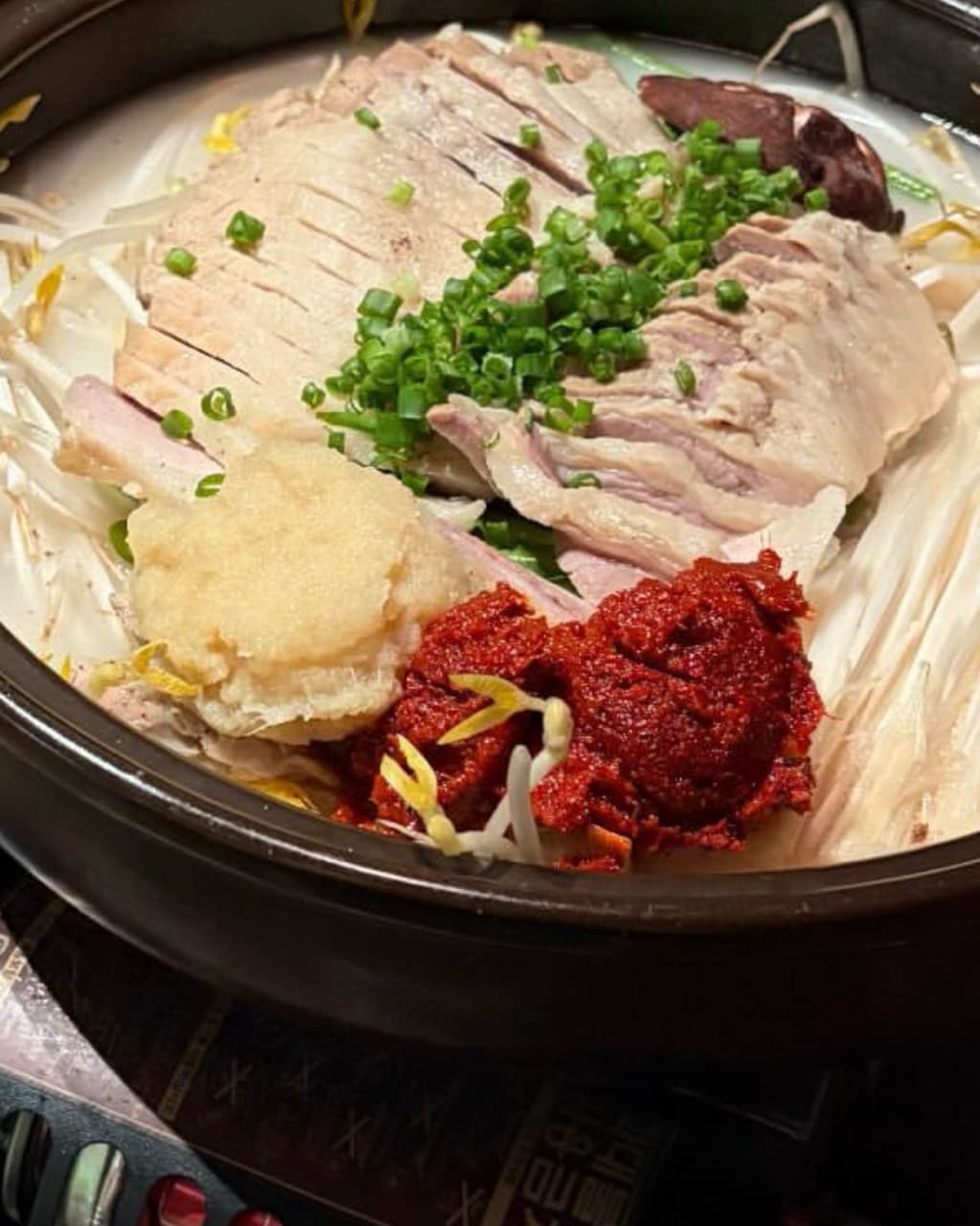 경기도 수원시 매산약수터 수원역본점 경기 요리주점 다찌석 1인 혼술 차림. 수육 고기 위로 다진 마늘과 양념장, 쪽파가 올라간 전골 냄비가 조명 아래 놓인 모습.