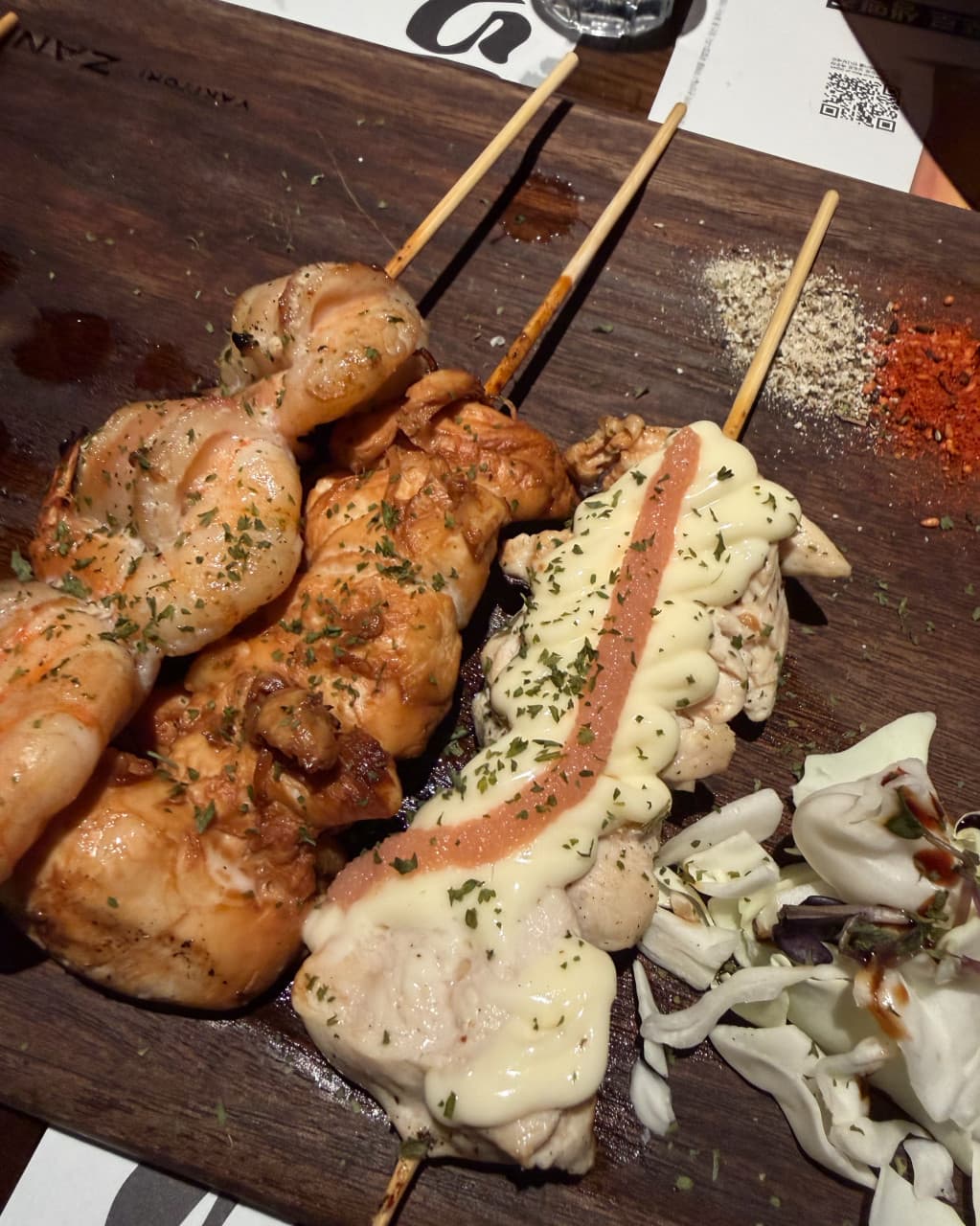 경기도 양주시 혼술 이자카야 야키토리잔잔 양주옥정점 경기 - 따뜻한 조명 아래 다찌석 나무판 위 명란 마요 닭꼬치와 소금, 시치미, 양배추가 놓인 상차림