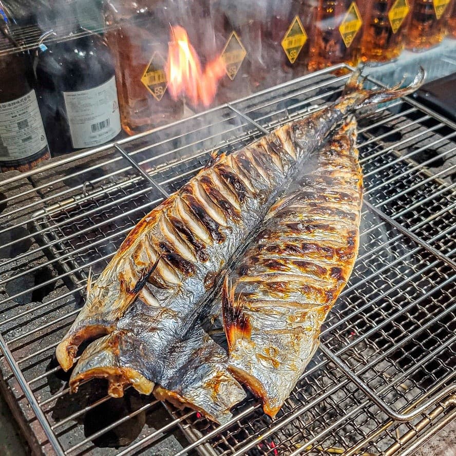 경기도 양주시 이자카야 야키토리잔잔 양주옥정점 경기 다찌석에서 보는 석쇠 위 직화 생선구이와 불길. 혼술 분위기 속 타오르는 연기와 노릇한 질감.