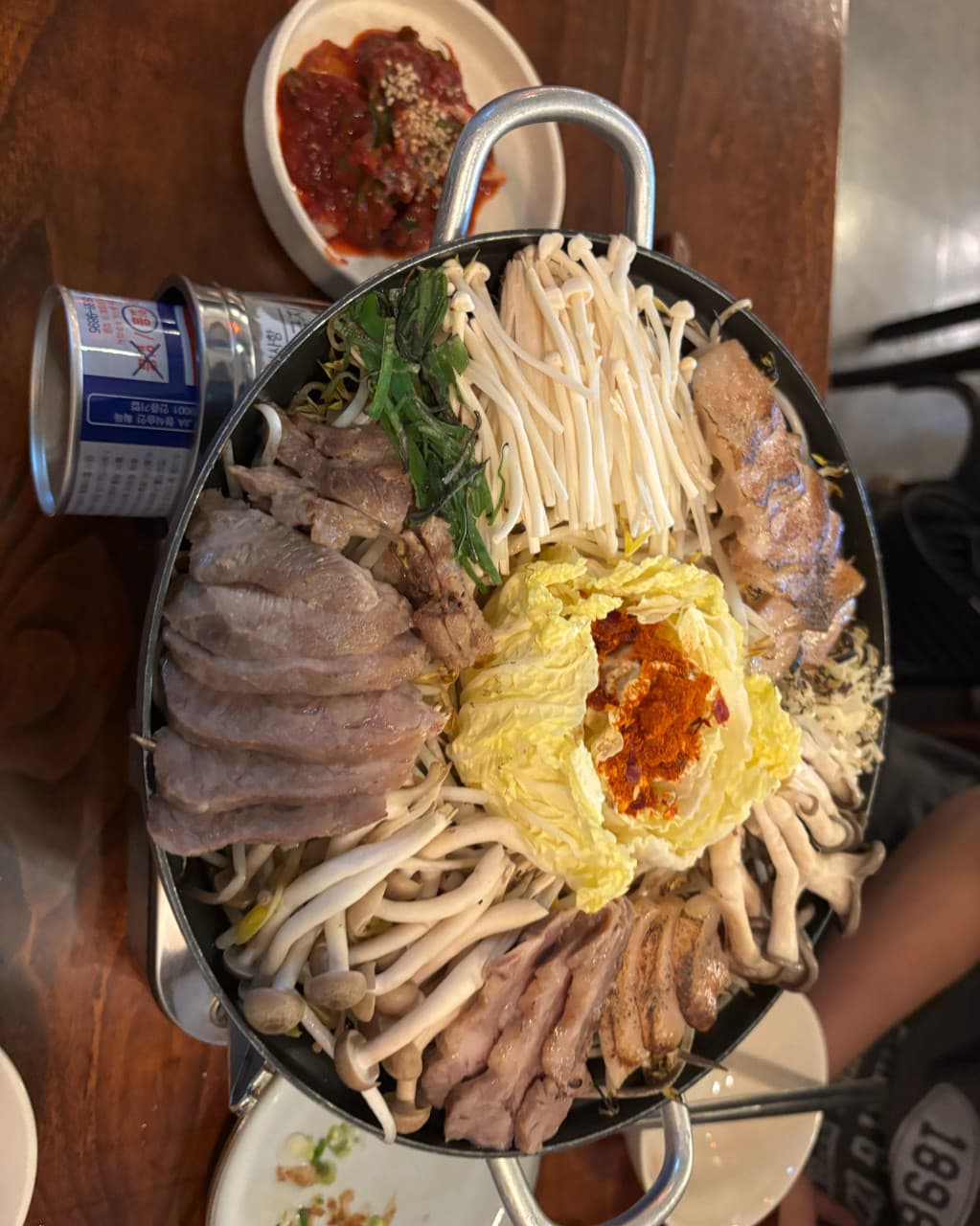 경기도 안양시 요리주점 이복실 경기 나무 테이블 위 고기와 버섯이 담긴 1인 전골. 다찌석 조명 아래 육류와 채소의 질감이 드러나는 혼술 상차림.