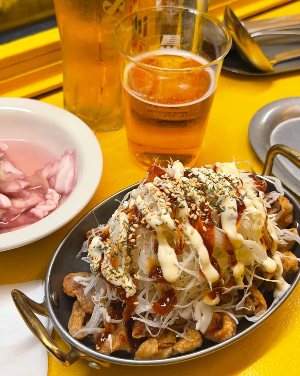경기도 성남시 요리주점 일편닭심 판교본점 경기 노란 조명 아래 1인 다찌석에서 생맥주와 소스 뿌린 양파 닭튀김 안주를 즐기는 혼술 상황