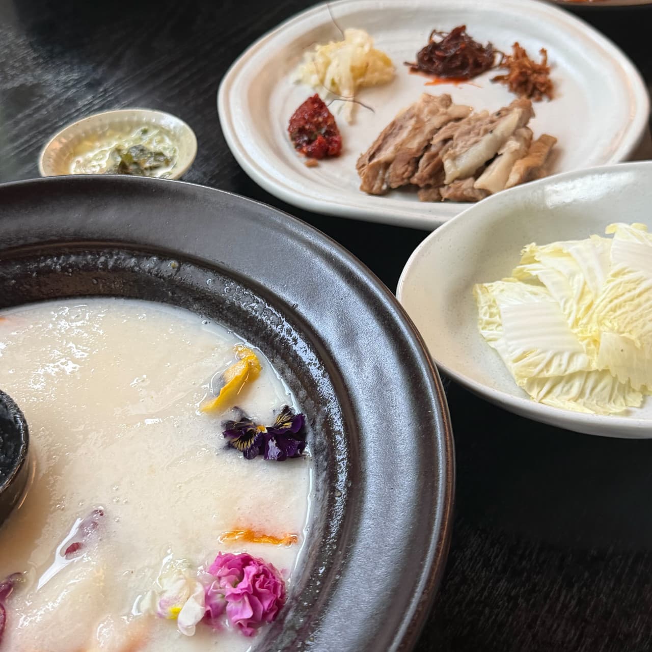 경기도 수원시 쌀술집 경기 요리주점 다찌석. 은은한 조명 아래 식용 꽃을 띄운 뽀얀 막걸리와 수육, 아삭한 배추가 차려진 1인 혼술 차림.