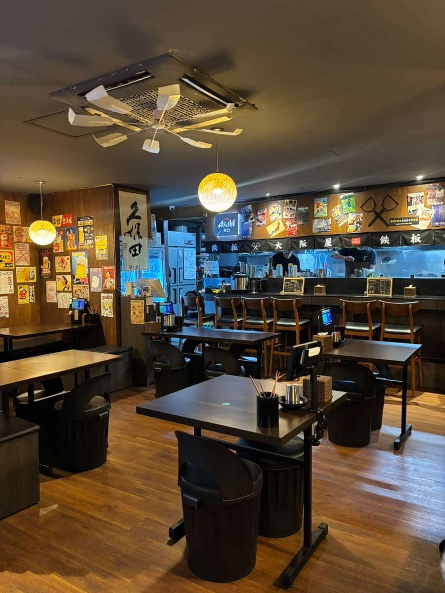 경기도 부천시 철판오사카야 부천점 경기 이자카야 - 노란 원형 조명 아래 1인 다찌석과 목제 테이블이 배치된 혼술 중심의 내부 공간 전경