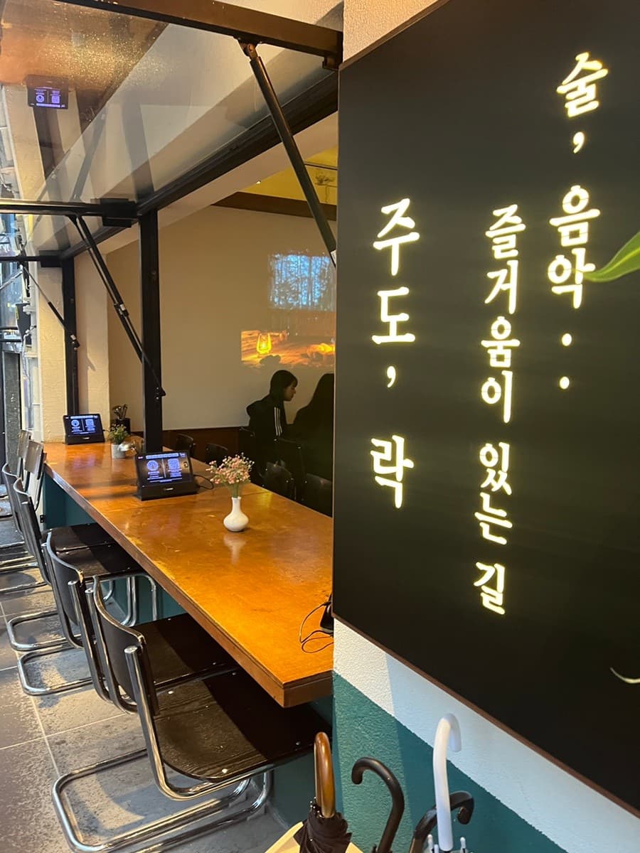 부산광역시 부산진구 요리주점 주도락 전포점 부산 - 빔프로젝터 영상이 나오는 벽면과 나무 다찌석, 1인 태블릿이 놓여 있는 혼술 공간