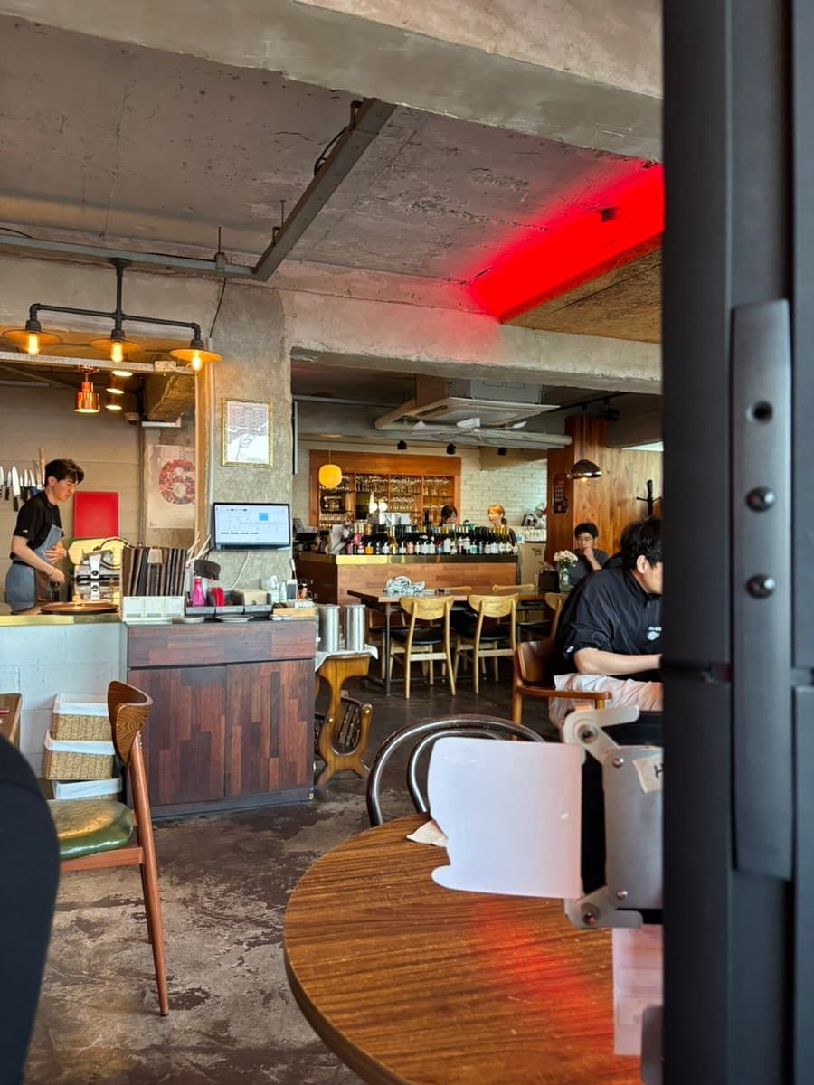 부산광역시 수영구 혼술 와인 광안리남매 부산 - 붉은 네온 조명 아래 1인 다찌석과 나무 테이블, 카운터에 진열된 와인병이 보이는 내부 구조