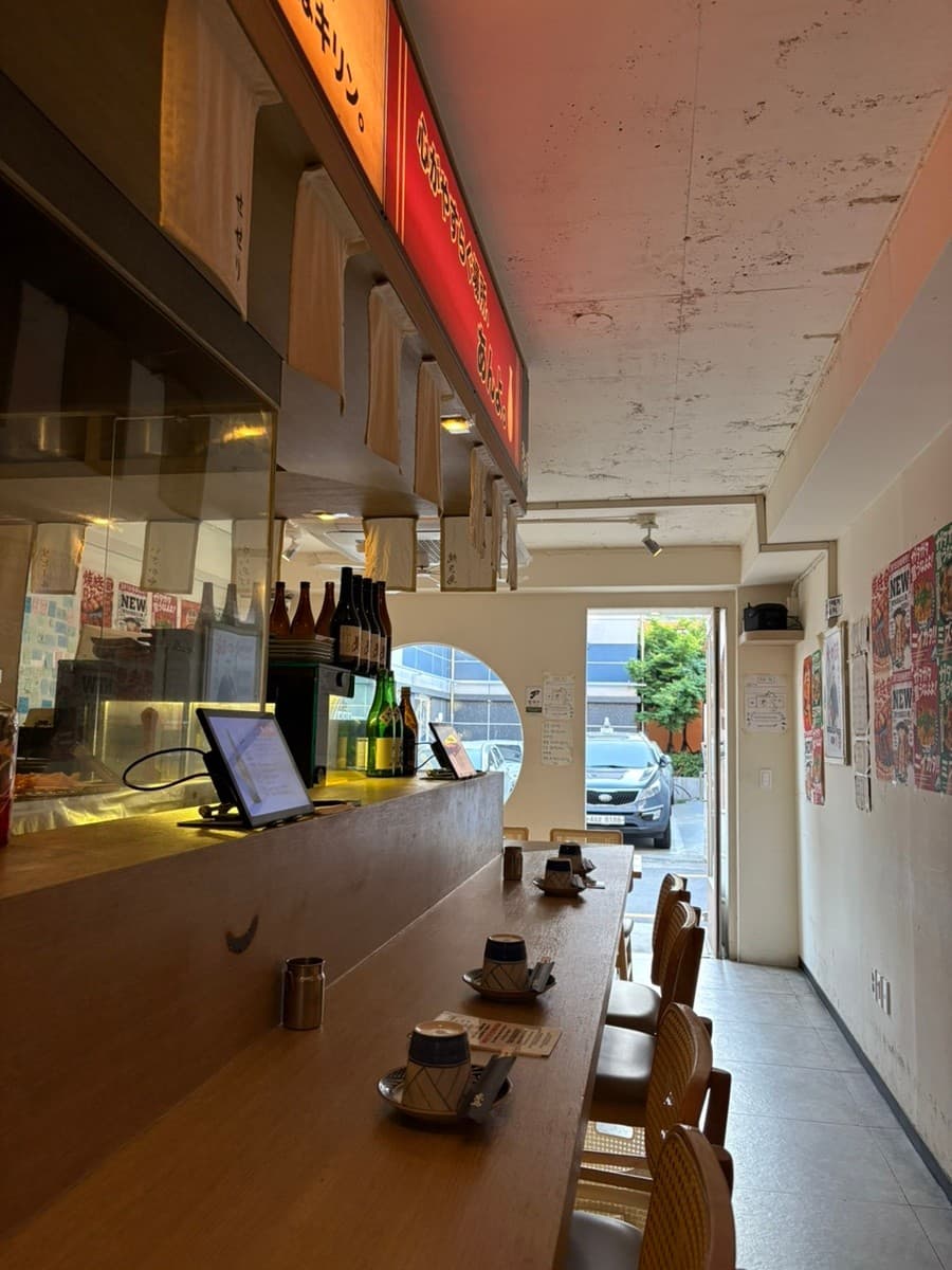 부산광역시 부산진구 요리주점 앙요 전포본점 부산. 주황색 조명 아래 원목 다찌석과 1인 식기, 주문용 태블릿이 배치된 혼술 공간.
