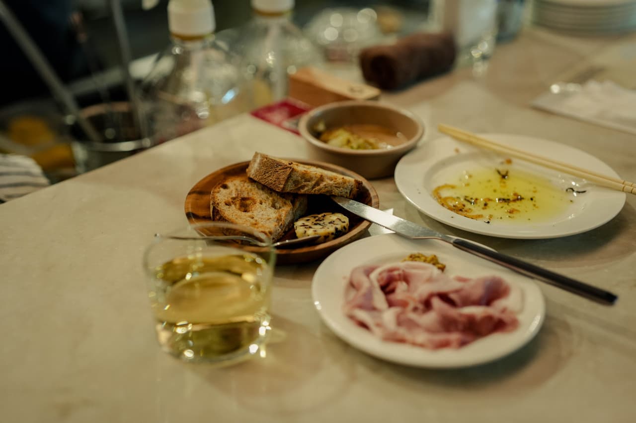 부산광역시 부산진구 솔티드웨이브 전포 부산 와인 바 다찌석 혼술. 노란 조명 아래 대리석 테이블 위 화이트 와인과 바게트, 햄, 오일 접시가 차려진 1인 좌석의 상황.