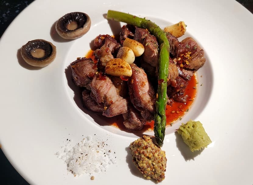 대구광역시 중구 배디스트 라운지 대구 1인 다찌석 혼술. 조명 아래 아스파라거스와 육즙 가득한 스테이크, 와사비가 담긴 흰 접시. 기타 라운지 바의 정갈한 안주 구성.