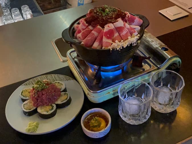 대구광역시 중구 도쿄테이스트 대구 이자카야 다찌석의 혼술 차림. 휴대용 가스레인지 위 소고기 전골과 육회 마키가 차려진 테이블에 어두운 조명과 푸른 불꽃이 대조를 이룸.