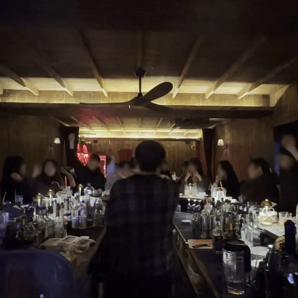 부산광역시 수영구 이자카야 블렌딩바 부산혼술바 광안리점의 낮은 조명 아래 다찌석에 앉은 혼술객들과 바 테이블 위 유리잔, 술병들이 배치된 내부 상황