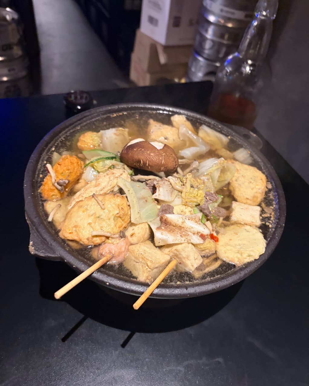 부산광역시 사하구 요리주점 다이닝도안 하단본점 부산. 조명 아래 다찌석에서 김이 나는 전골 속 버섯과 오뎅 꼬치를 혼술하며 즐기는 상황.