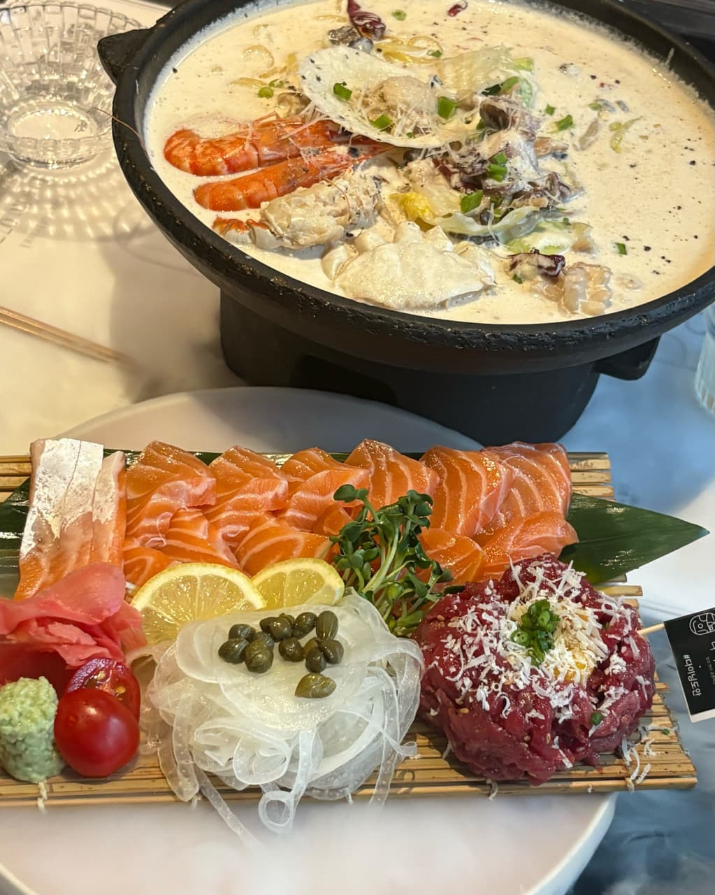부산광역시 사하구 요리주점 다이닝도안 하단본점 부산의 조명 아래 1인 연어 사시미와 육회 세트. 다찌석에서 크림 해물 나베의 질감을 느끼며 혼술을 즐기는 상황.