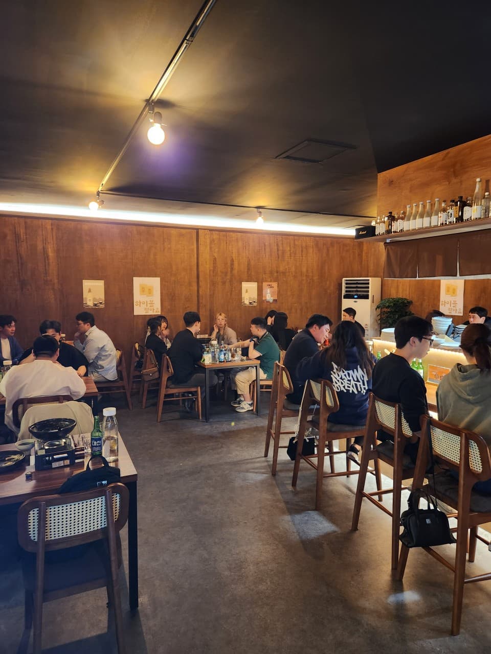 부산광역시 동래구 요리주점 월하주방 부산 - 전구색 조명 아래 목재 인테리어와 1인 다찌석에서 하이볼과 소주를 즐기는 혼술 분위기