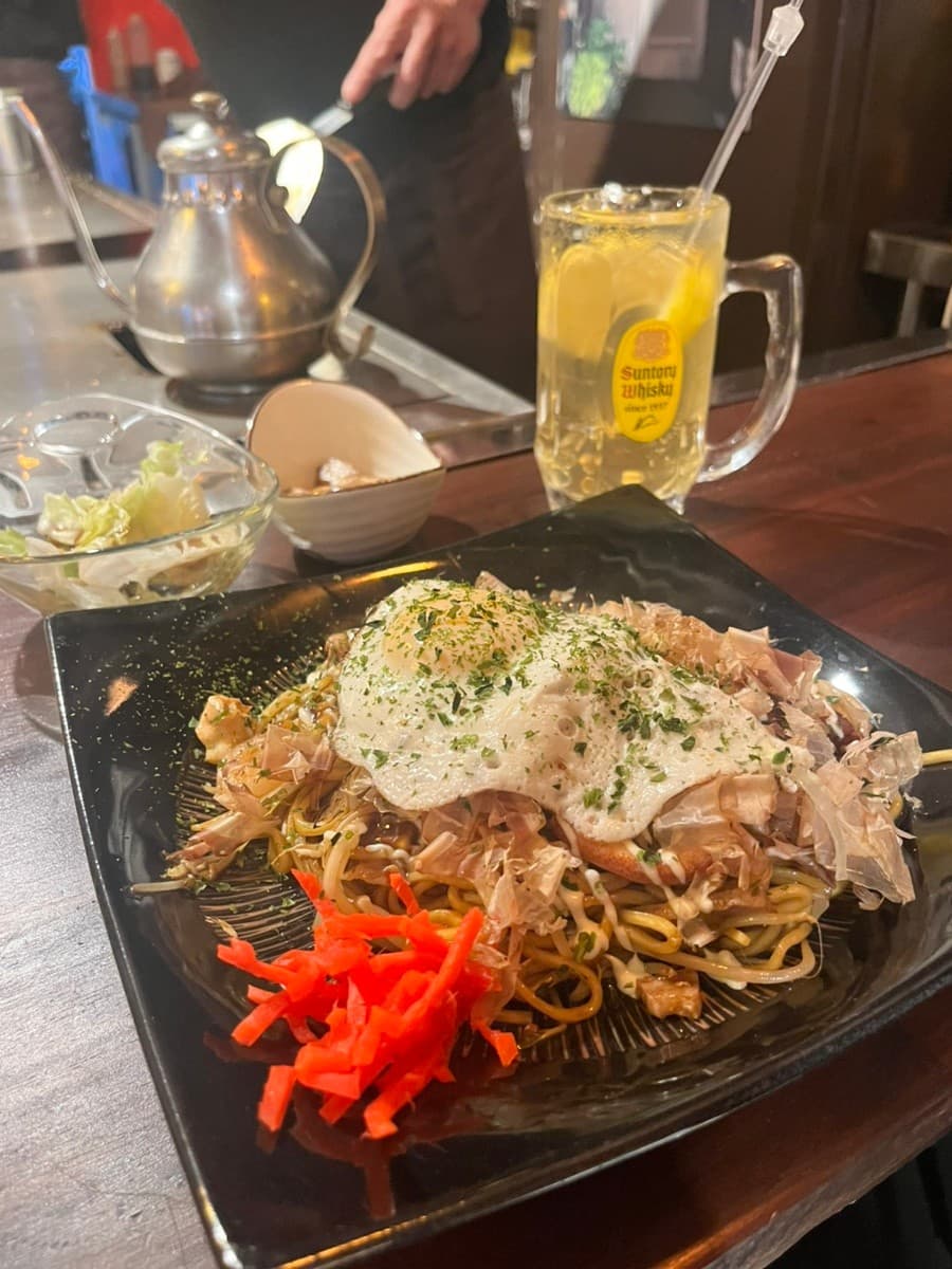 부산광역시 부산진구 요리주점 데판킹 부산 1인 다찌석. 노란 조명 아래 철판에서 조리된 야키소바와 가쓰오부시, 계란프라이, 레몬 하이볼이 차려진 혼술 상황.