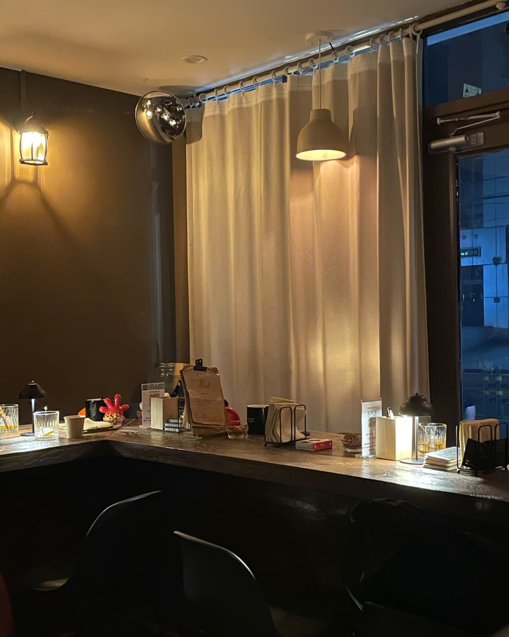 부산광역시 수영구 곁 부산혼술바 광안리점 바(Bar)의 노란 조명 아래 나무 다찌석과 술잔. 혼술을 위한 1인 좌석과 흰 커튼이 배치된 실내 구성.