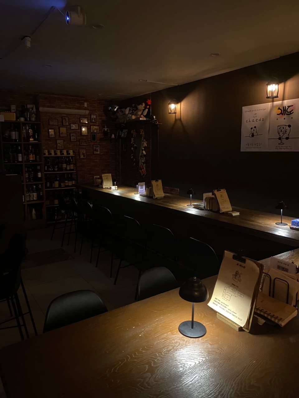 부산광역시 수영구 곁 부산혼술바 광안리점 바(Bar) - 어두운 조명 아래 긴 나무 다찌석과 1인 혼술용 개별 스탠드 및 메뉴판이 비치된 내부 전경