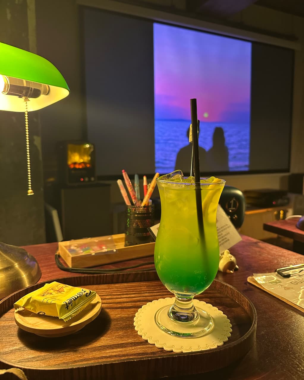 부산광역시 수영구 광안리골방 부산 바(Bar)의 초록색 조명 아래 놓인 1인 혼술 좌석. 목재 트레이 위 그라데이션 칵테일과 대형 스크린 속 노을 영상이 비치는 다찌석 공간.