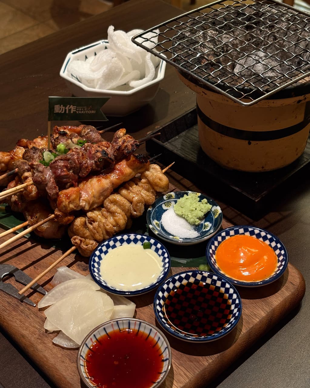 인천광역시 남동구 이자카야 야키토리동작 인천시청점 혼술 차림. 나무 도마 위 닭꼬치와 미니 화로, 다섯 가지 소스가 담긴 종지들이 노란 조명 아래 놓인 1인 다찌석 풍경.
