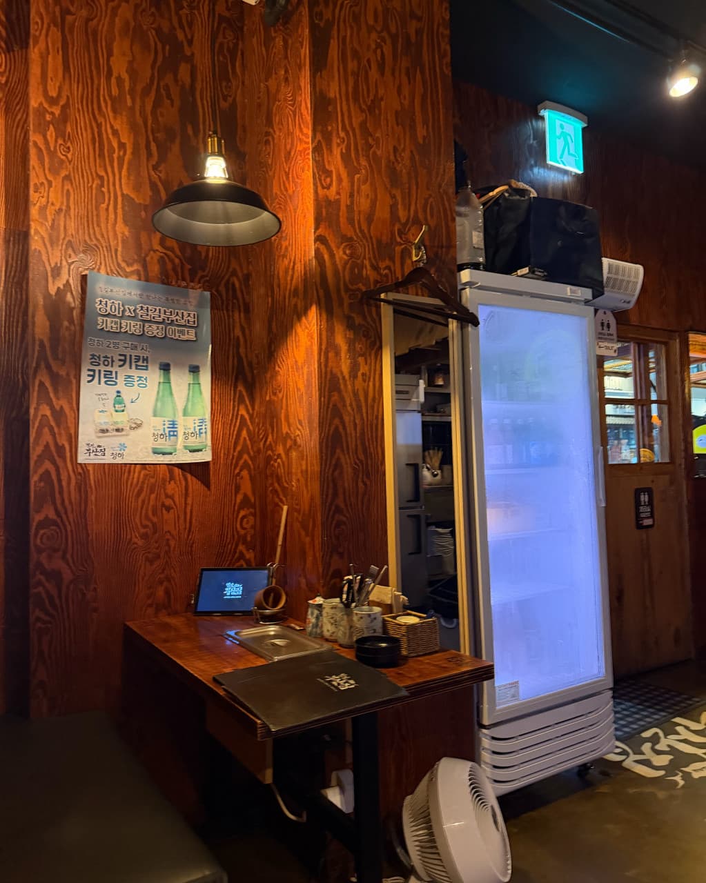 인천광역시 연수구 요리주점 철길부산집 송도타임스페이스점 인천 내부. 노란 조명 아래 나무 소재 다찌석과 태블릿이 설치된 1인 혼술 좌석. 메뉴판과 식기류가 정돈된 테이블 구성을 보여줌.