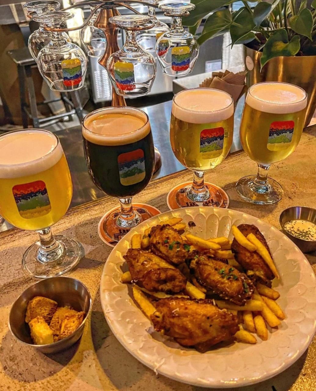 제주특별자치도 서귀포시 혼술 맥주,호프 제주약수터 - 조명 아래 1인 다찌석에 차려진 수제 맥주 네 잔과 바삭한 치킨 윙, 감자튀김