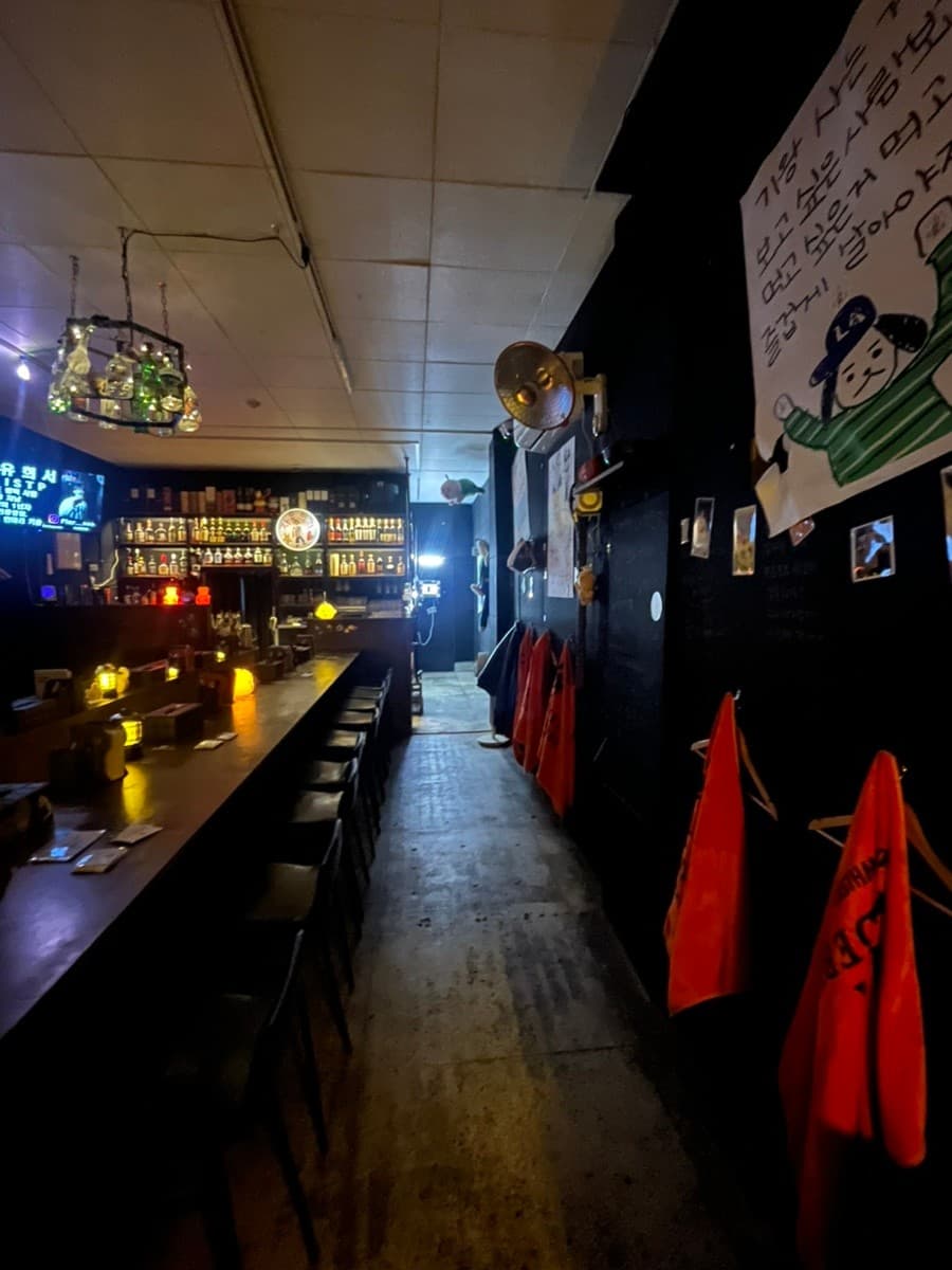 제주특별자치도 제주시 자유의지 혼술바 제주본점 바(Bar)의 어두운 조명 아래 놓인 긴 다찌석과 1인용 좌석이 혼술 분위기를 조성함.
