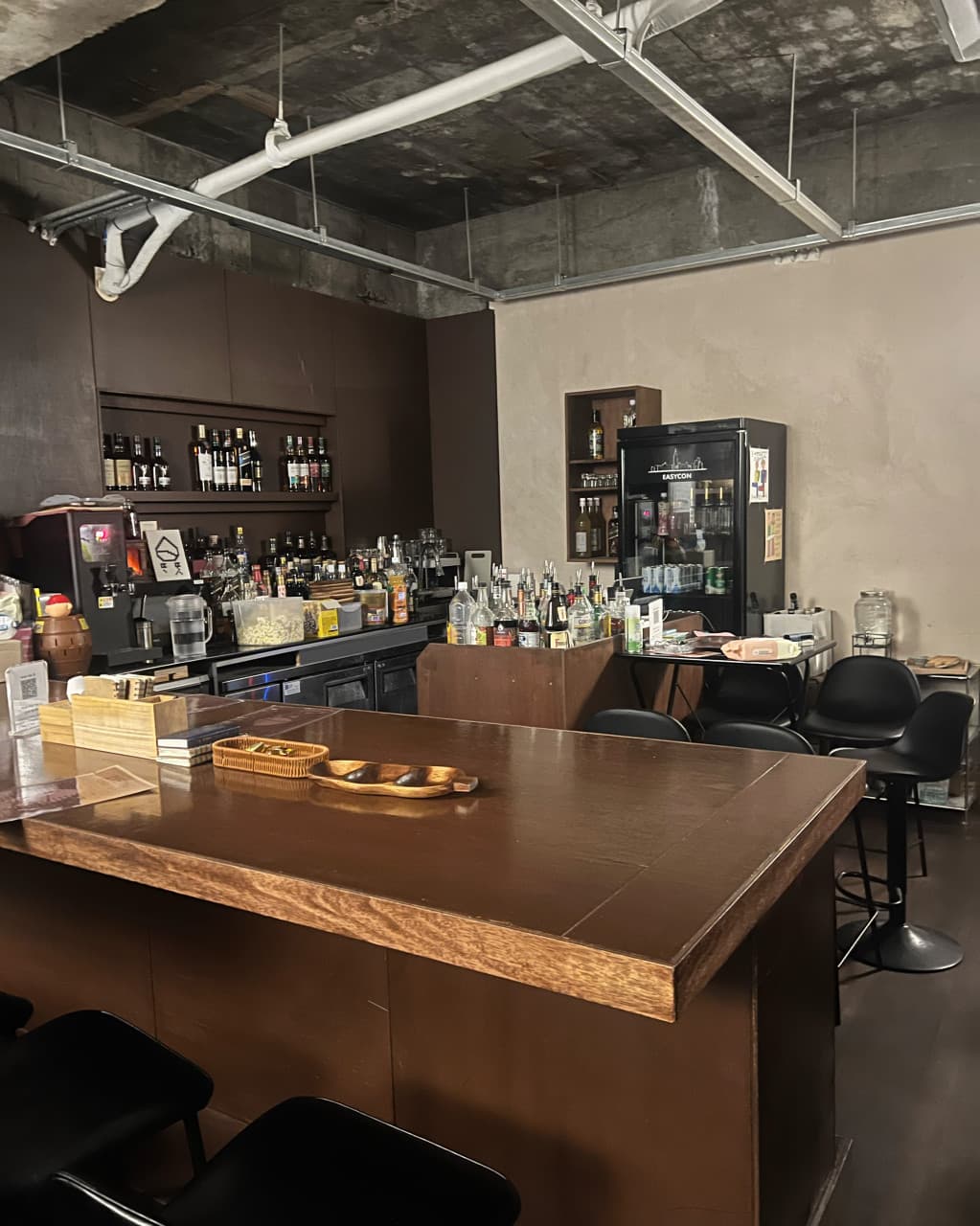 제주특별자치도 제주시 또똣 제주혼술바 바(Bar)의 긴 원목 다찌석과 1인용 바 스툴. 조명 아래 선반 가득 진열된 위스키 병들과 노출 천장이 보이는 혼술 공간을 보여줌.