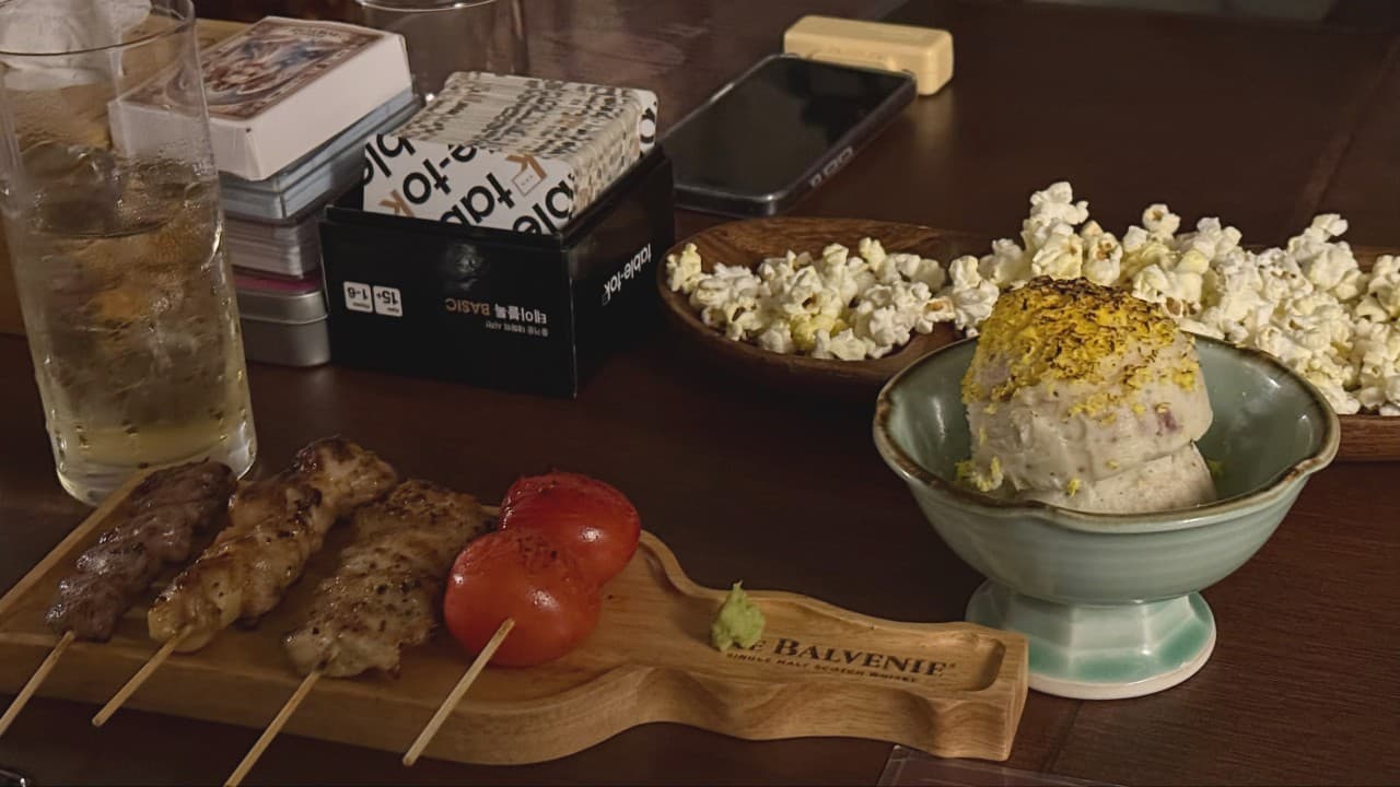 제주특별자치도 제주시 또똣 제주혼술바 바(Bar) 다찌석의 낮은 조명 아래 닭꼬치와 감자샐러드, 하이볼이 차려진 1인 테이블에서 혼술을 즐기는 상황.