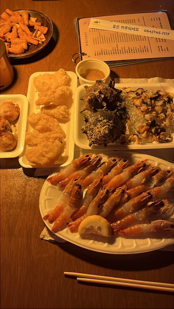 제주특별자치도 제주시 단지 제주혼술바 바(Bar) 다찌석 조명 아래 놓인 1인 딱새우회와 뿔소라 사시미 세트. 혼술을 위해 정갈하게 담긴 해산물과 튀김이 차려진 테이블