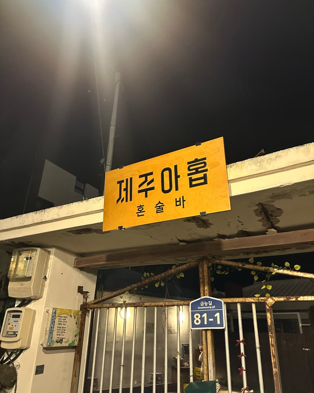 제주특별자치도 제주시 제주아홉 혼술바 본점 협재점 바(Bar) 입구. 밤 가로등 조명 아래 노란 나무 간판과 철제 대문이 위치한 1인 혼술 공간의 외관.