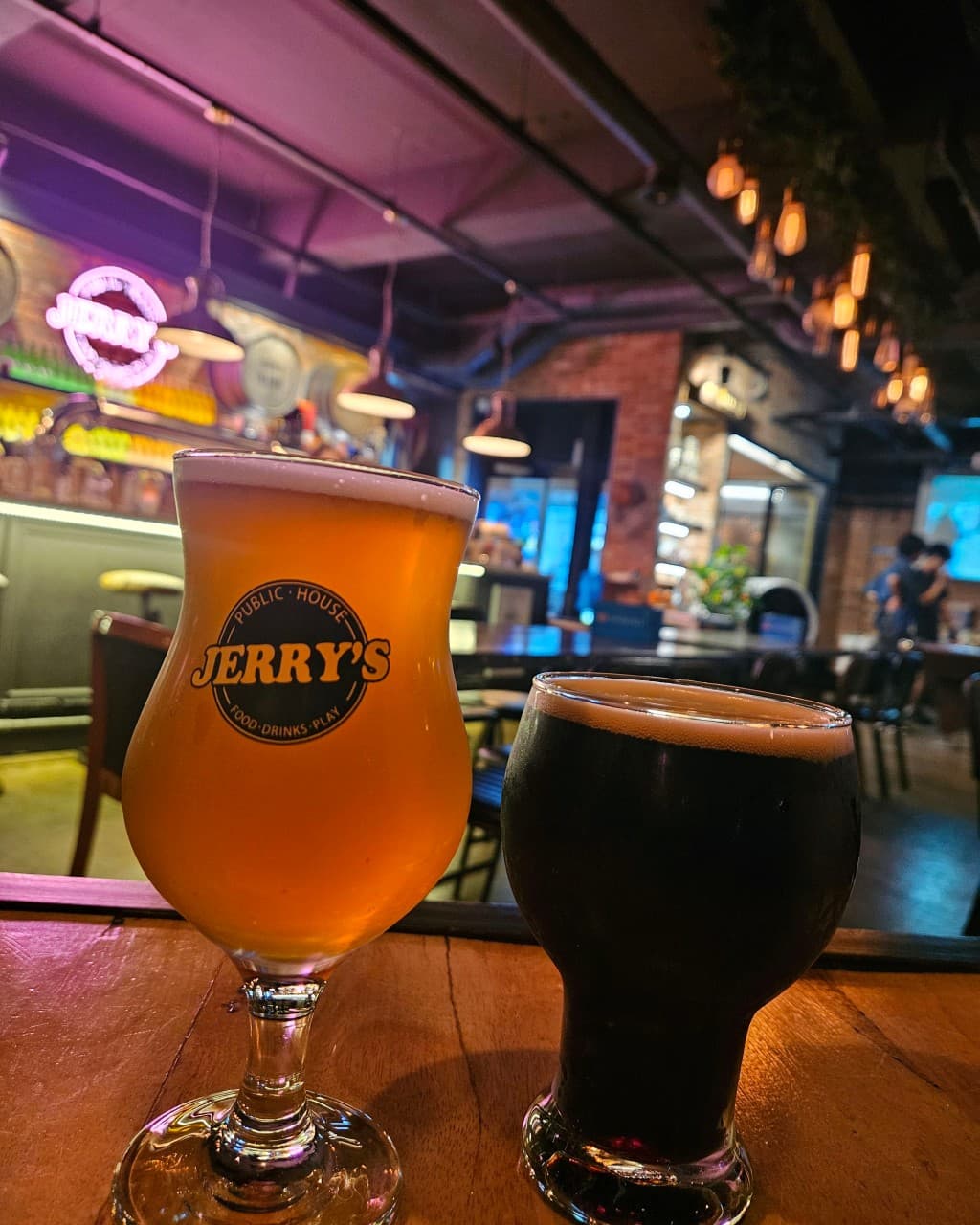 제주특별자치도 서귀포시 제리스펍 제주서귀포점 맥주 호프 다찌석 위 거품이 올라온 생맥주와 흑맥주. 보라색 네온 조명과 전구가 빛나는 공간에서 혼술을 하는 상황.