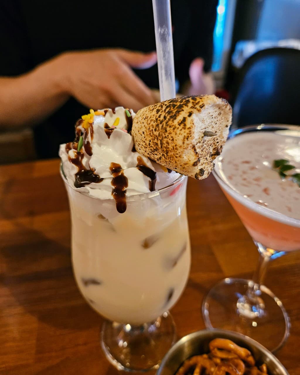 대전광역시 동구 혼술 바(Bar) 공강 대전 - 조명 아래 1인 테이블 위 구운 마시멜로와 생크림을 얹은 칵테일, 분홍색 음료와 프레첼이 놓인 상황