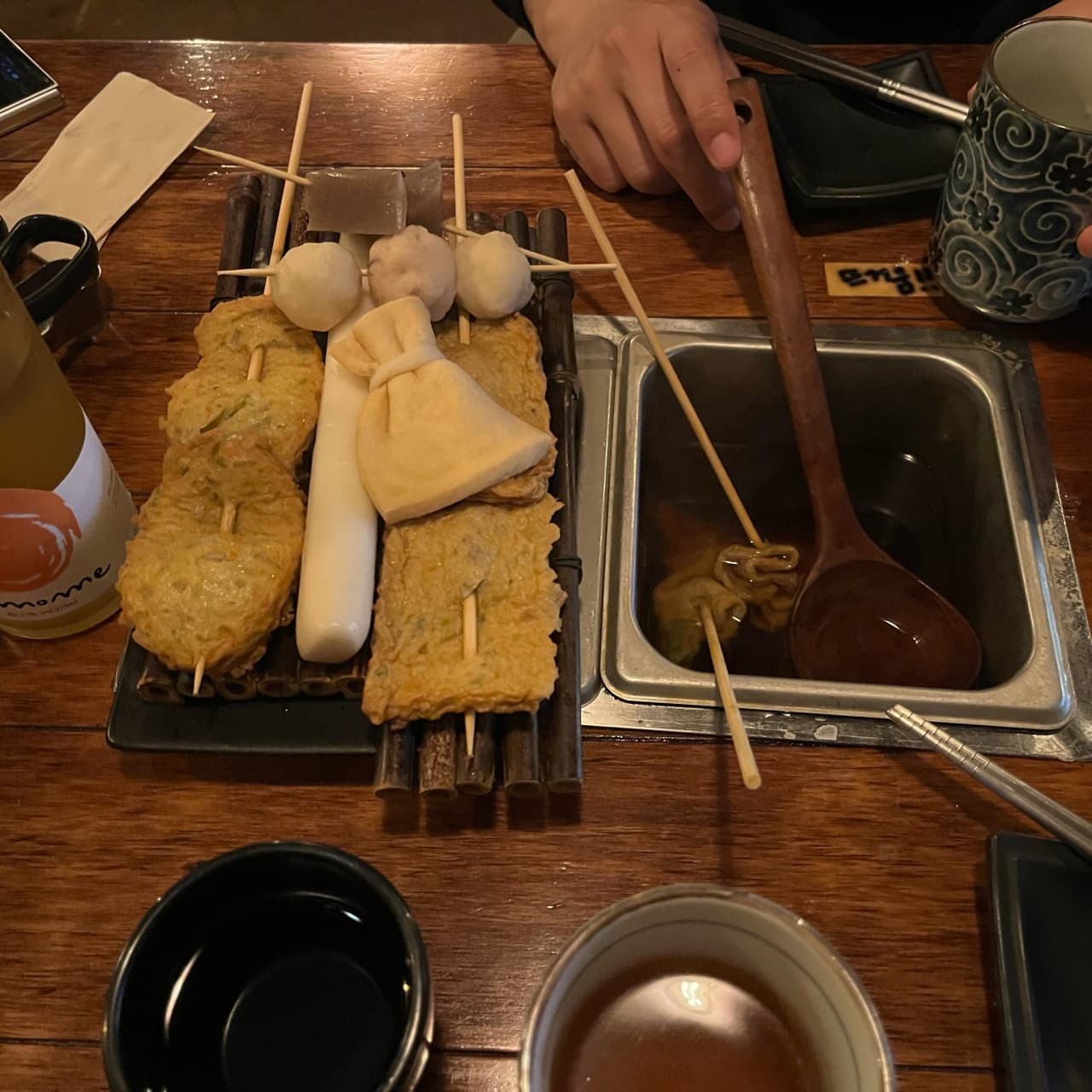대전광역시 서구 요리주점 철길부산집 대전관저점 나무 식탁 위 모둠 어묵과 육수통이 있는 1인 혼술 자리. 나무 국자와 도자기 컵이 놓인 다찌석 상황.