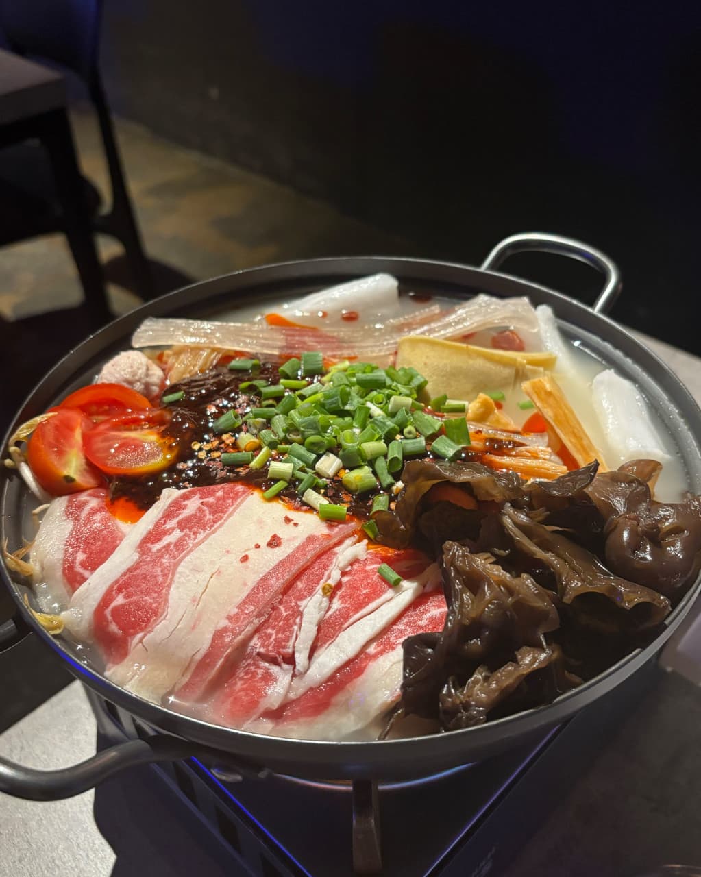 대전광역시 서구 요리주점 연주 대전의 1인 혼술 다찌석 위 선홍빛 소고기와 목이버섯, 토마토가 담긴 전골. 어두운 실내 조명이 비추는 냄비 속 다양한 식재료와 육수의 질감.