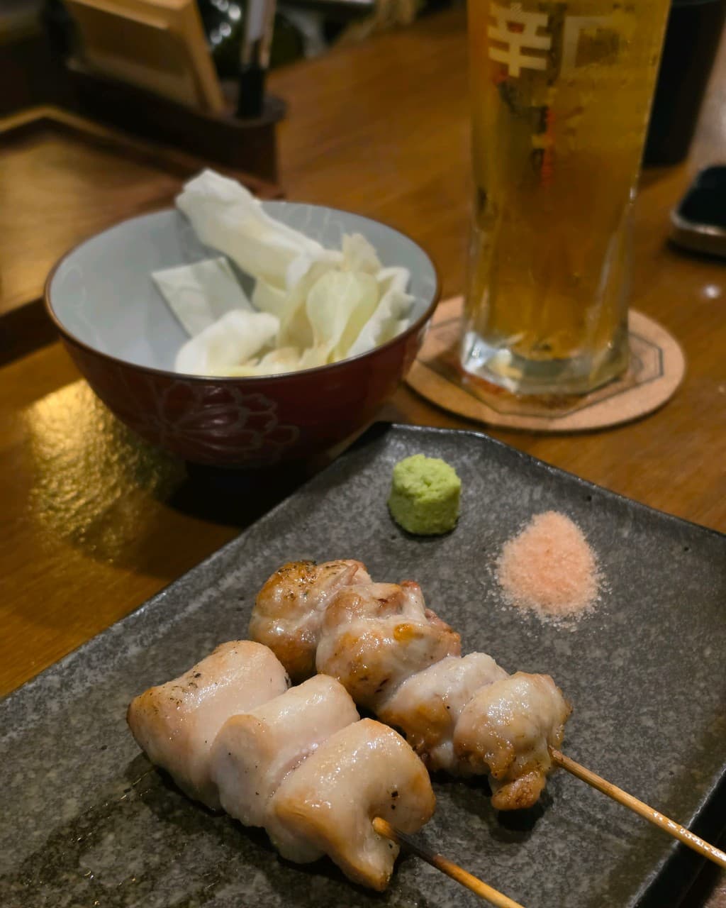 대전광역시 서구 토사카 대전 이자카야 다찌석에 차려진 닭꼬치 구이와 생맥주. 와사비와 핑크 솔트가 놓인 검은 접시와 양배추가 포함된 혼술 차림.