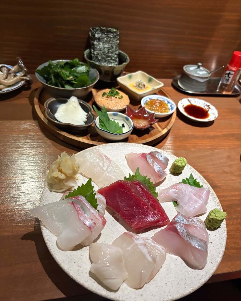 대전광역시 서구 이자카야 로바타모에 목재 다찌석 위 은은한 조명을 받는 1인 사시미 세트. 윤기 나는 생선회와 김, 여러 찬이 차려진 혼술 구성을 보여줌.