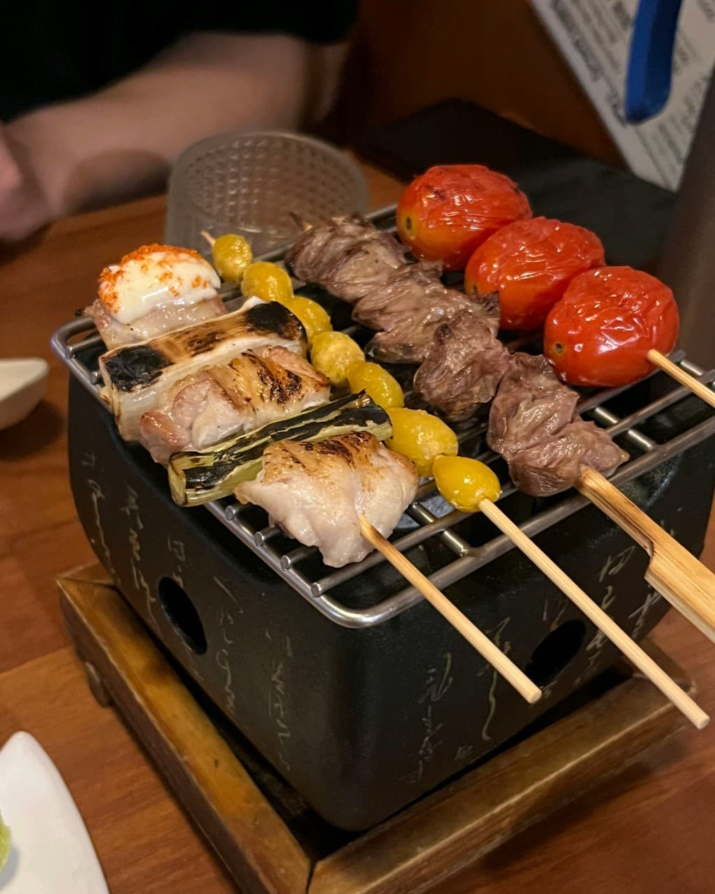 대전광역시 동구 이자카야 모테키 대전 - 다찌석 1인 화로 위 토마토와 닭고기 꼬치구이. 조명 아래 구워진 대파와 은행의 질감이 드러난 혼술 테이블.