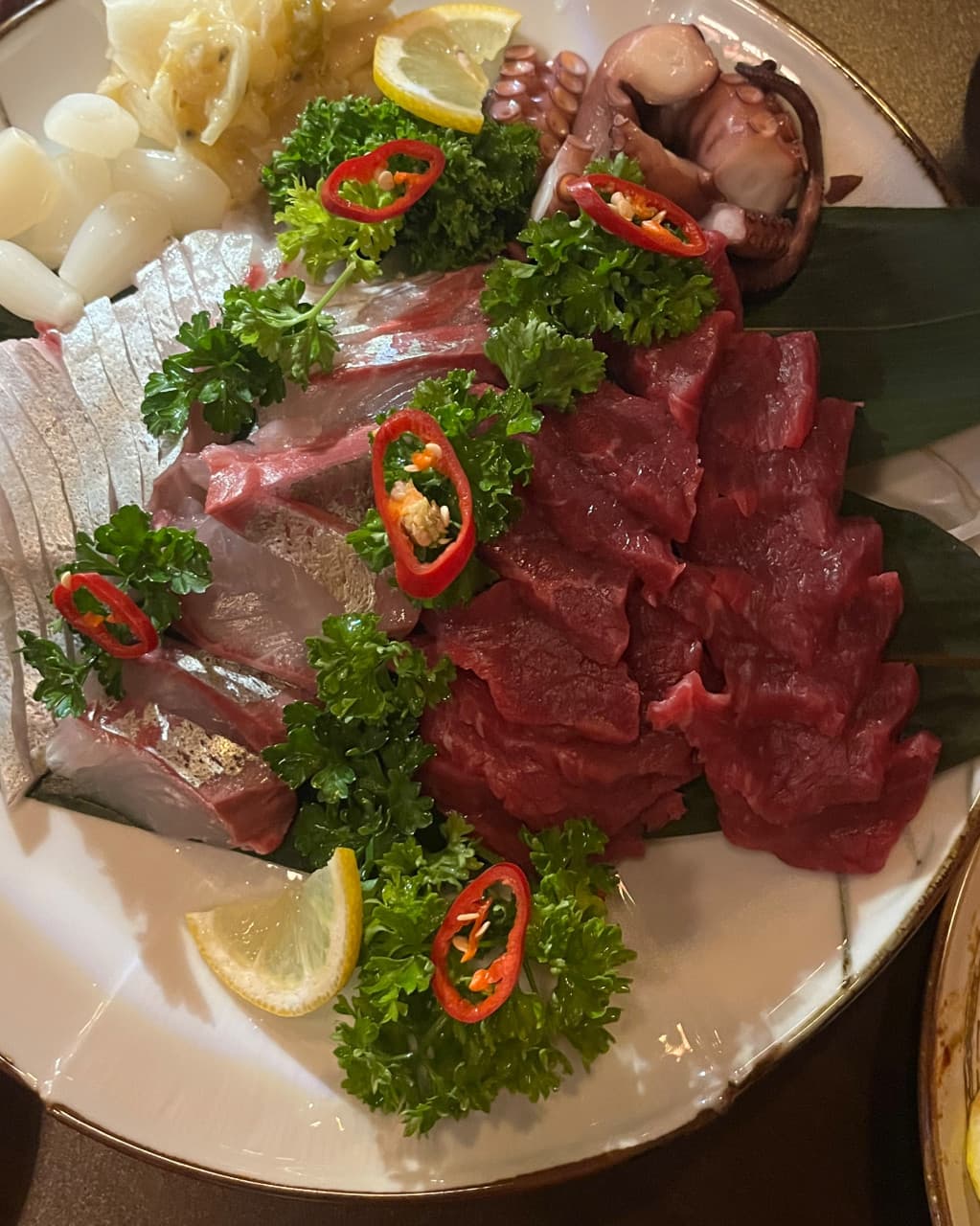 대전광역시 유성구 나루 봉명점 대전 이자카야 다찌석의 조명과 1인 사시미. 선홍빛 육사시미와 문어숙회의 질감이 혼술 상황을 잘 나타냄.
