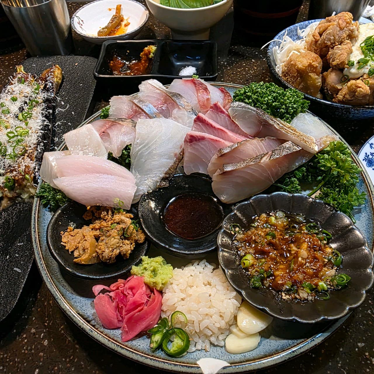 경기도 수원시 나츠비 율전동본점 경기 이자카야 다찌석 조명 아래 1인 사시미와 가라아게. 혼술 상황에 맞춰 차려진 두툼한 회의 질감과 구운 가지 요리 구성.