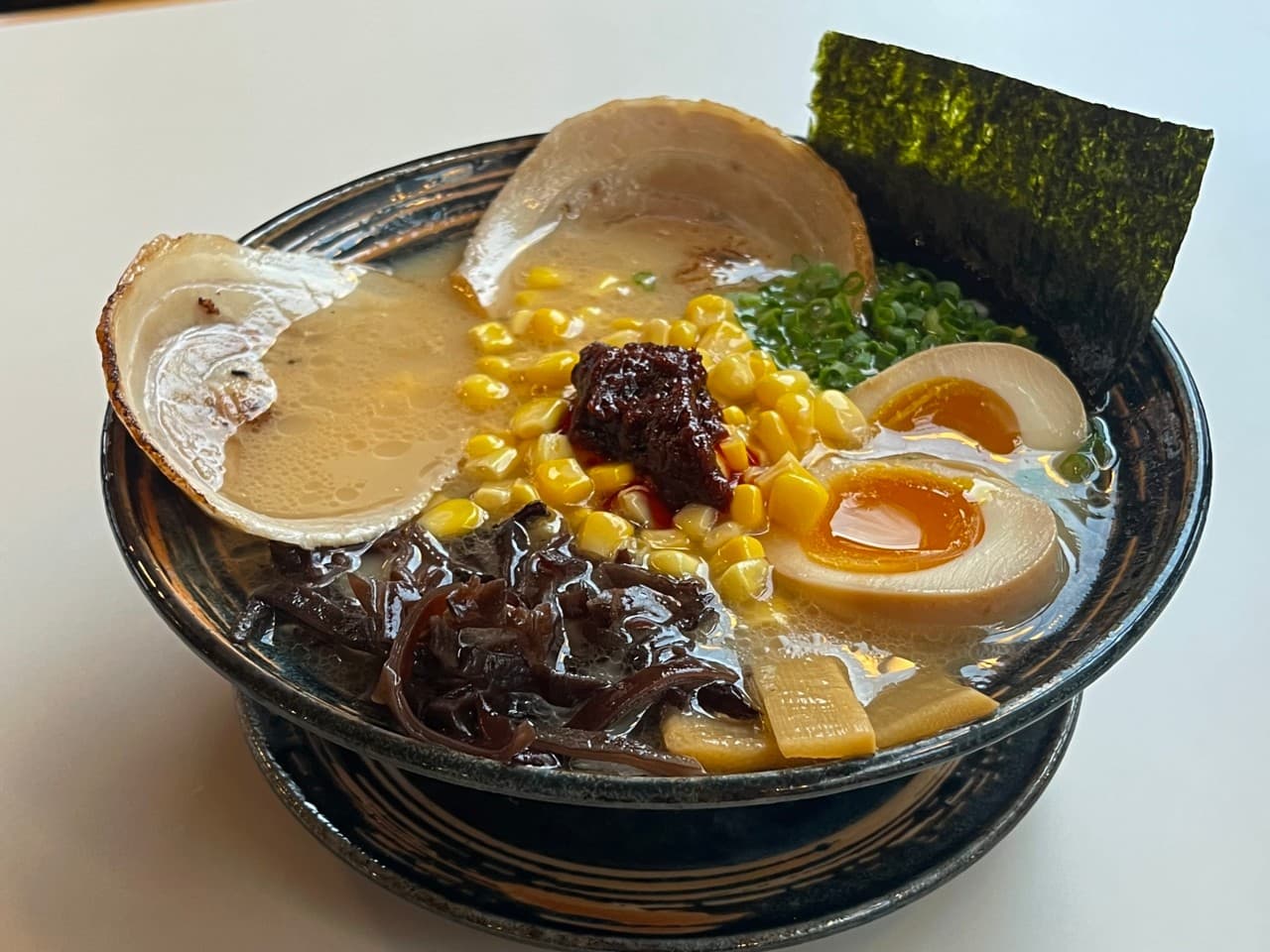 경기도 안양시 요리주점 마시타 경기 다찌석 조명 아래 차슈와 반숙란, 옥수수 토핑을 얹은 1인 라멘. 혼술 상황의 식재료 질감과 식기 배치를 상세히 묘사.