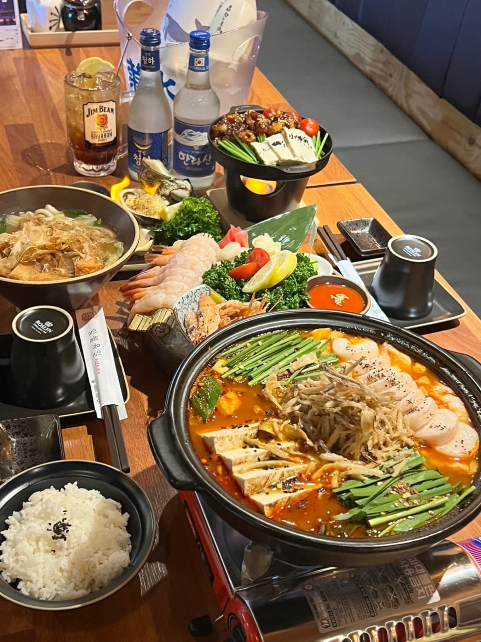 경기도 고양시 일월육일 일산점 경기 이자카야 다찌석 위 붉은 국물의 모츠나베와 단새우 사시미. 노란 조명 아래 하이볼과 소주가 차려진 1인 혼술 상차림.