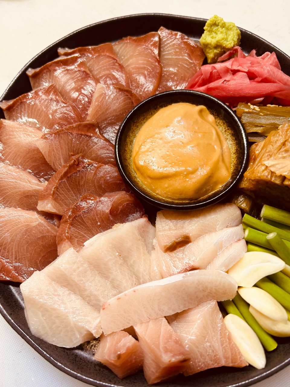 경기도 성남시 이자카야 키리모리 본점 경기 다찌석 조명 아래 놓인 1인 사시미. 윤기 흐르는 생선회와 중앙의 소스, 마늘종이 담긴 접시로 조용한 혼술 상황을 연출함.