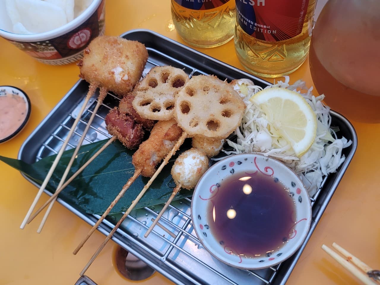 경기도 안산시 이자카야 숯토리 안산고잔점 경기. 노란 테이블 다찌석에 차려진 바삭한 연근과 치즈 쿠시카츠 꼬치 튀김, 맥주가 놓인 1인 혼술 상황.