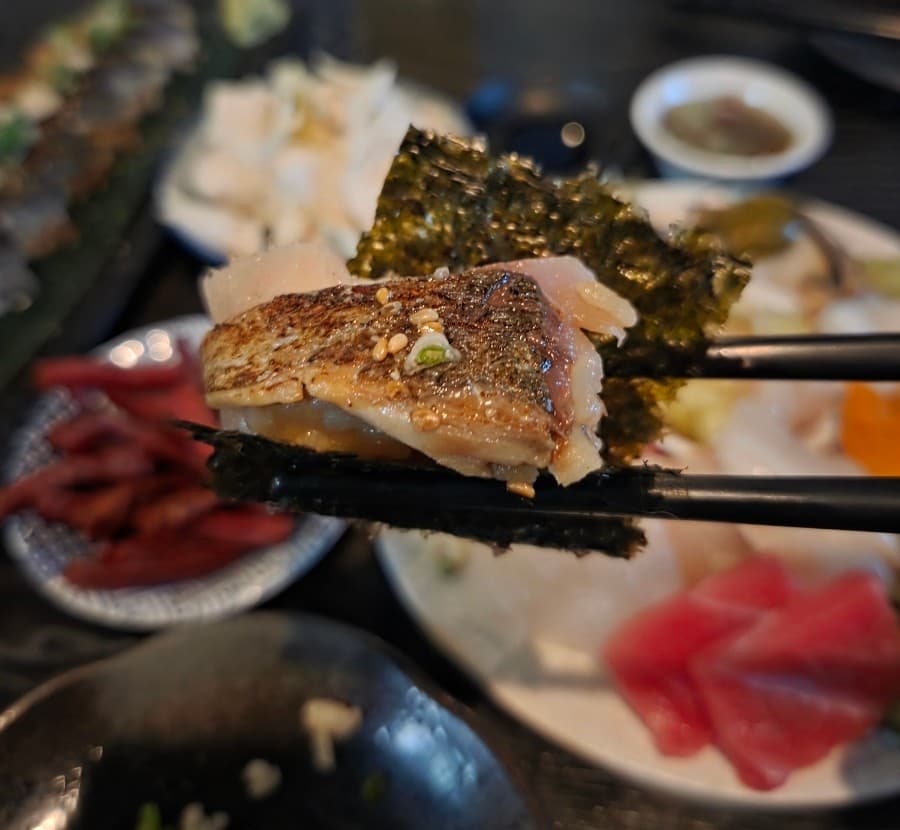 대구광역시 수성구 로지우라 대구 이자카야 다찌석 혼술. 조명 아래 젓가락으로 든 김과 고등어의 질감, 배경의 1인용 사시미가 차려진 상황을 보여줌.