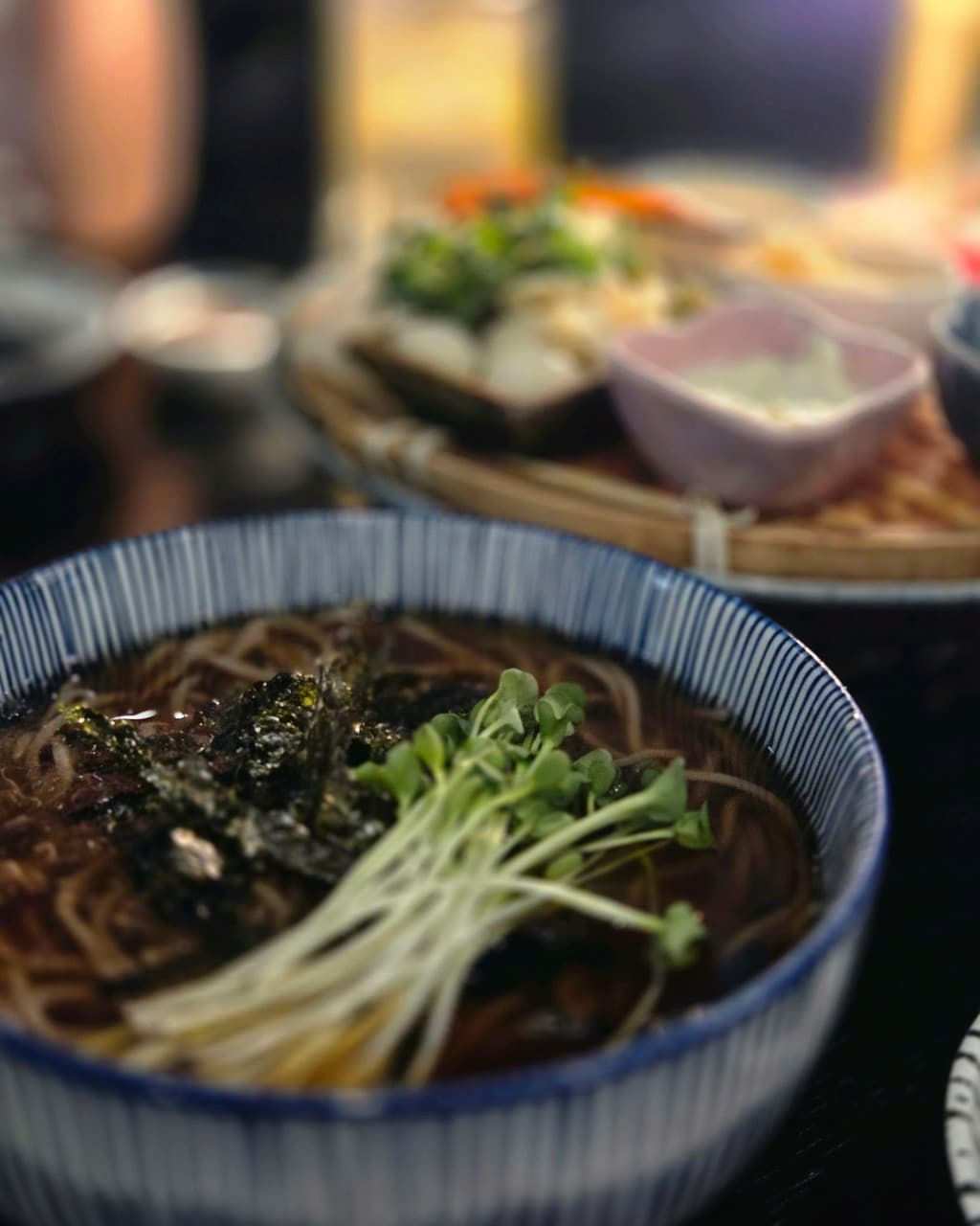 대구광역시 달성군 대담히 다사점 대구 이자카야 다찌석 1인 혼술. 무순과 김가루가 올라간 소바와 나무 소반에 담긴 안주들이 조명 아래 배치된 상황.